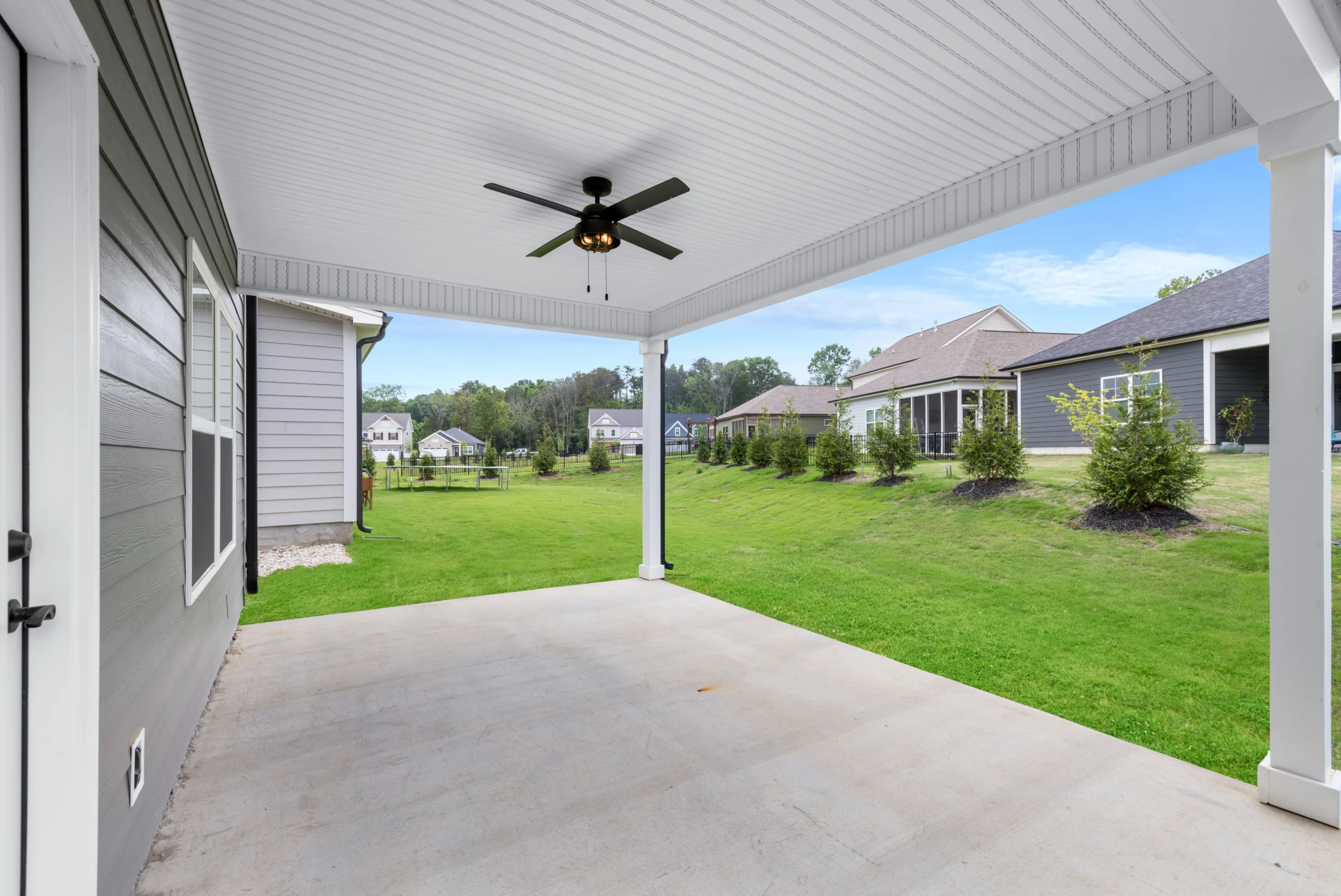 New Home Chattanooga TN. Covered patio with ceiling fan overlooks grassy backyard, surrounded by modern homes by Pratt Home Builders.