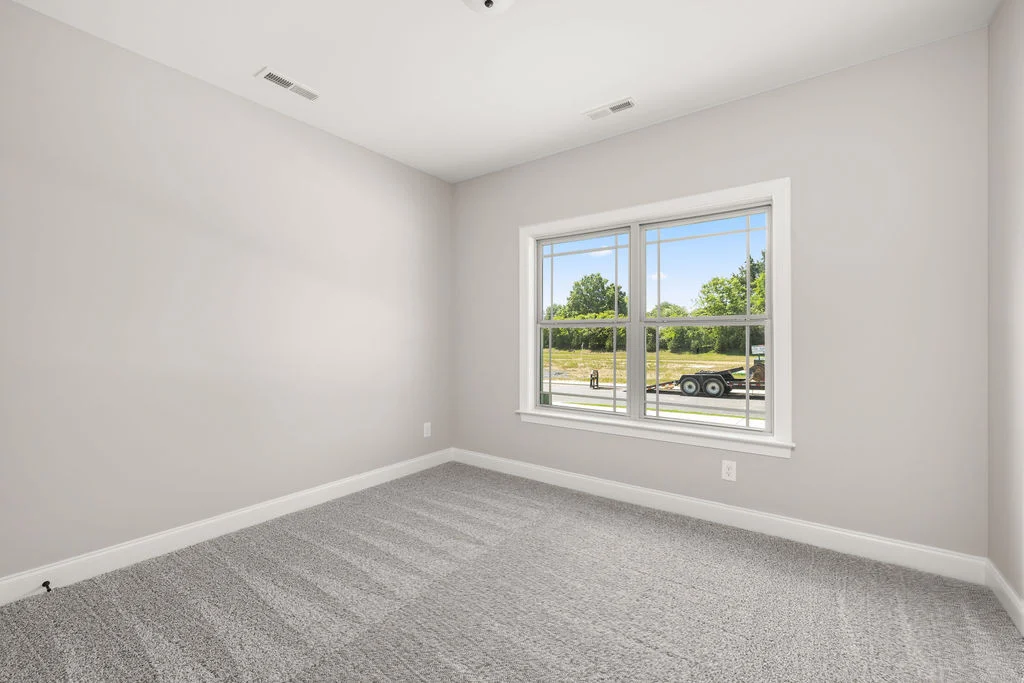 Empty room with light gray walls, carpet, and a large window overlooking a green landscape by Pratt Home Builders in Chattanooga TN.