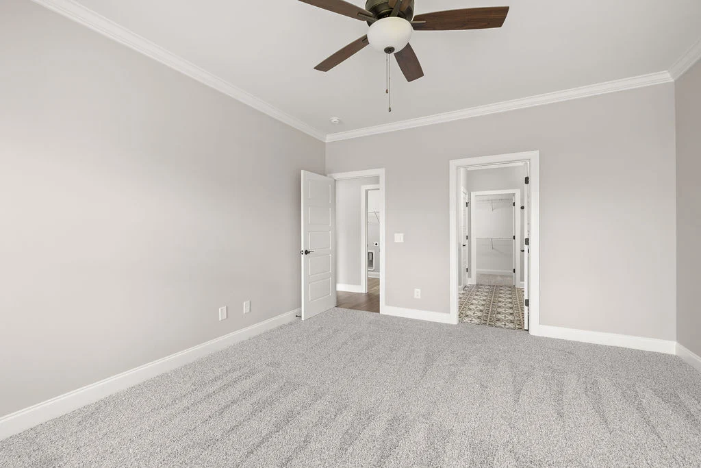 New Home Chattanooga. Spacious, neutral-toned room with carpet, ceiling fan, and two open doors leading to adjacent spaces by Pratt Home Builders.