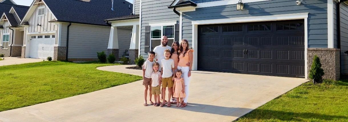 ridgesong (1) Family of six smiling in front of a modern home by Pratt Home Builders in Chattanooga TN, surrounded by lush green lawns.
