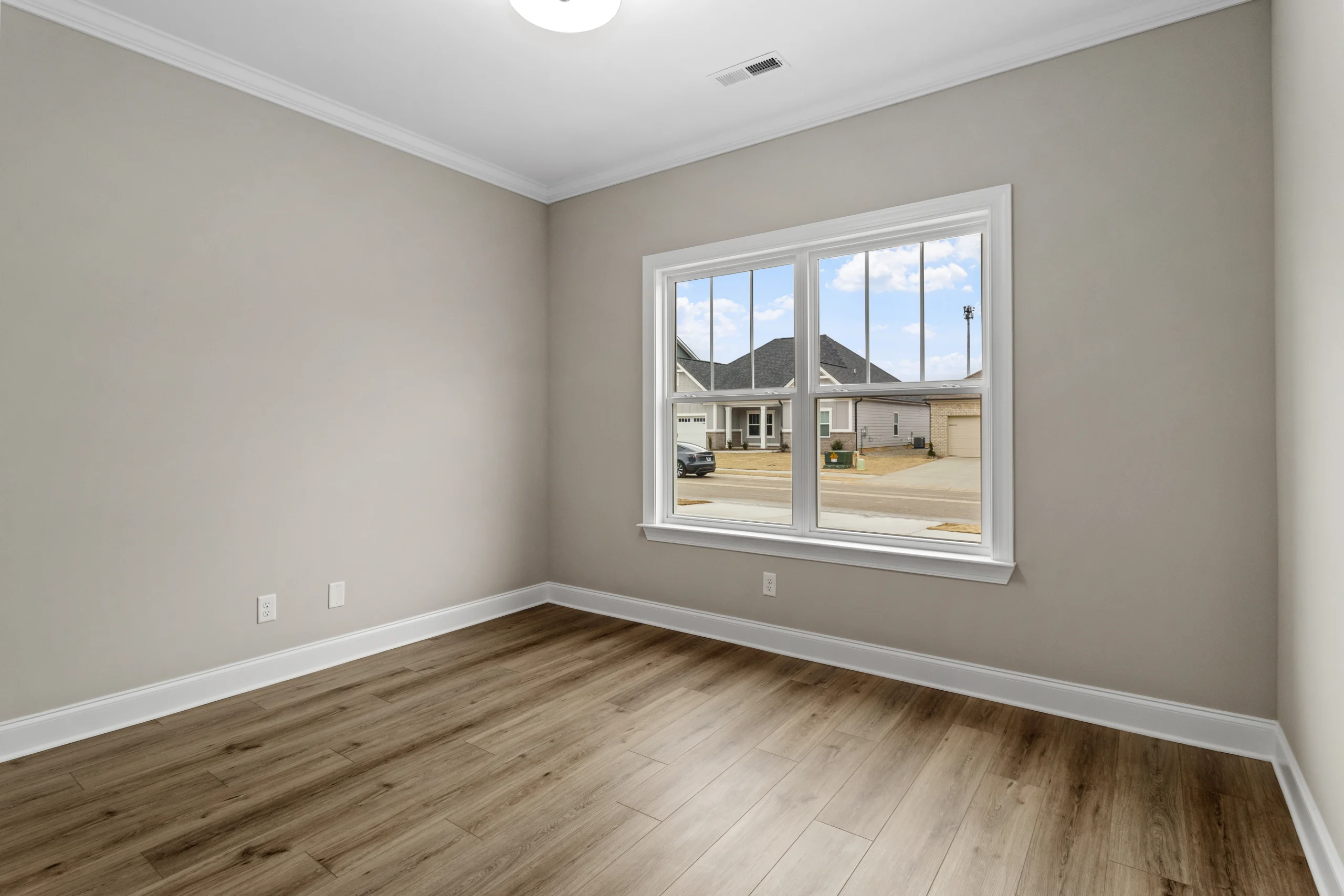New Home Chattanooga TN. Empty room with light wood flooring, large window, and beige walls, showcasing Pratt Home Builders' interior design.