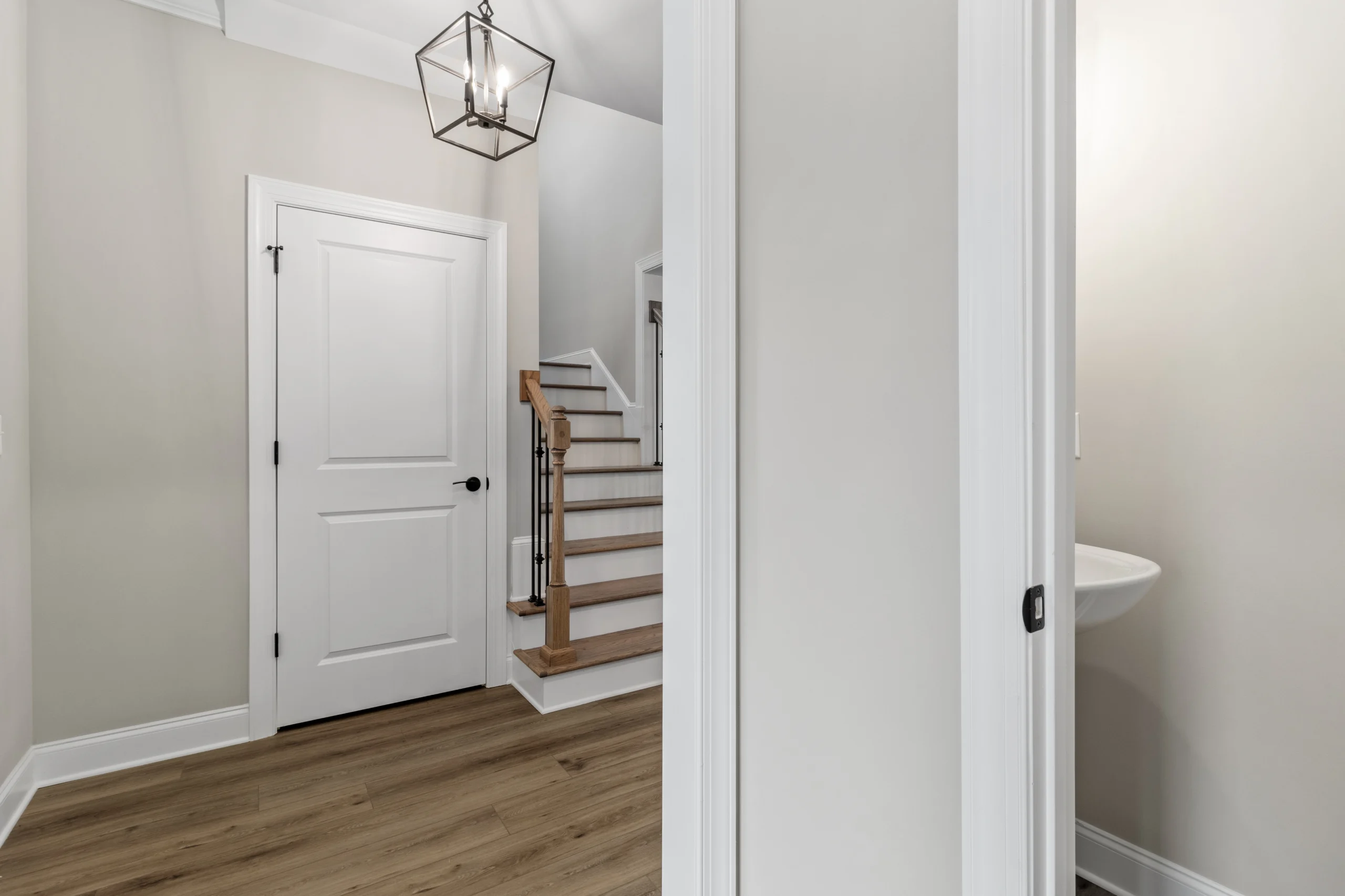 New Home Chattanooga TN. Modern hallway with light wood flooring, white doors, staircase, and pendant light, designed by Pratt Home Builders.