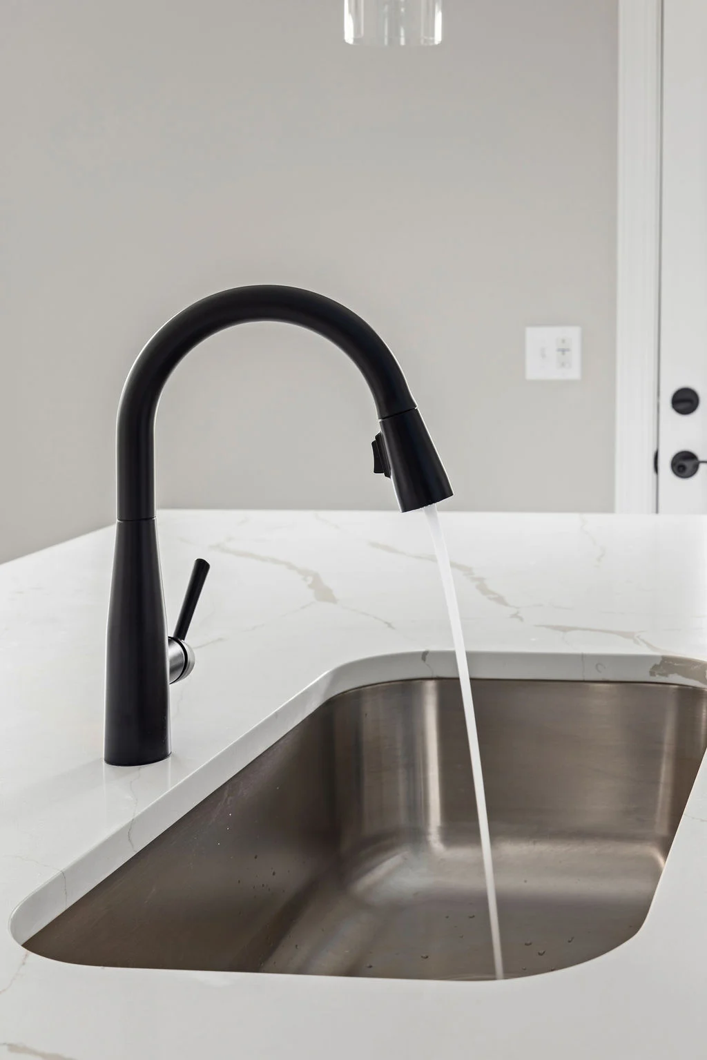 Modern black faucet with water flowing into a stainless steel sink, set on a white marble counter by Pratt Home Builders in Chattanooga TN.