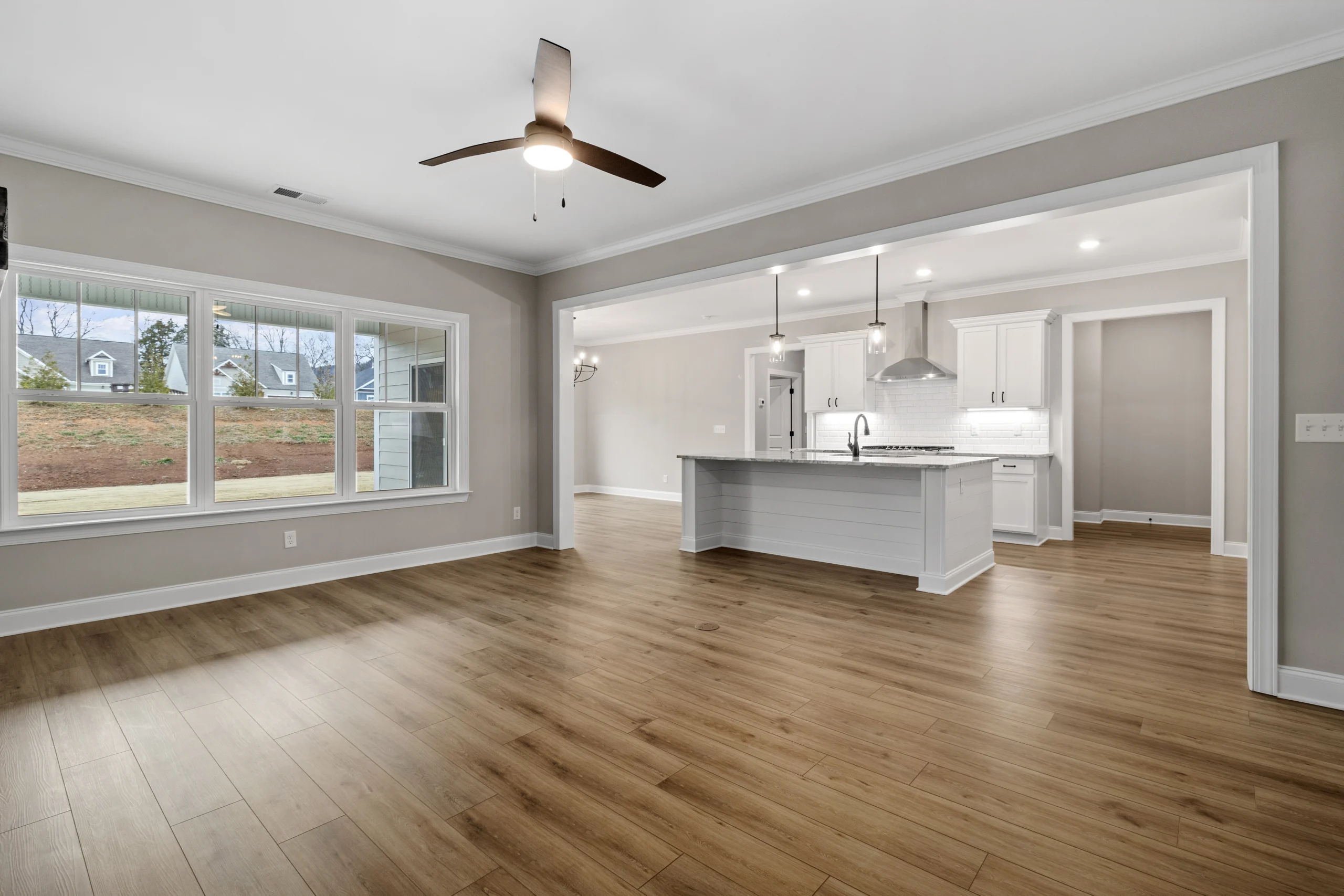 New Home Chattanooga TN. Spacious open-concept living area with wood floors, large window, and modern kitchen by Pratt Home Builders.