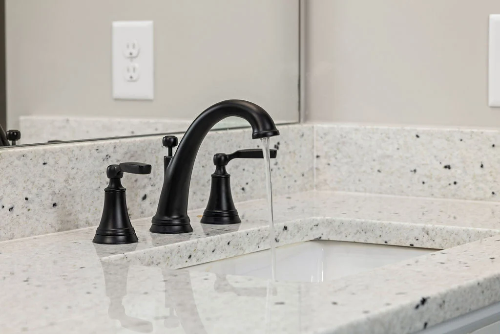 Sleek black bathroom faucet with granite countertop by Pratt Home Builders in Chattanooga TN. Water flowing gently into sink.