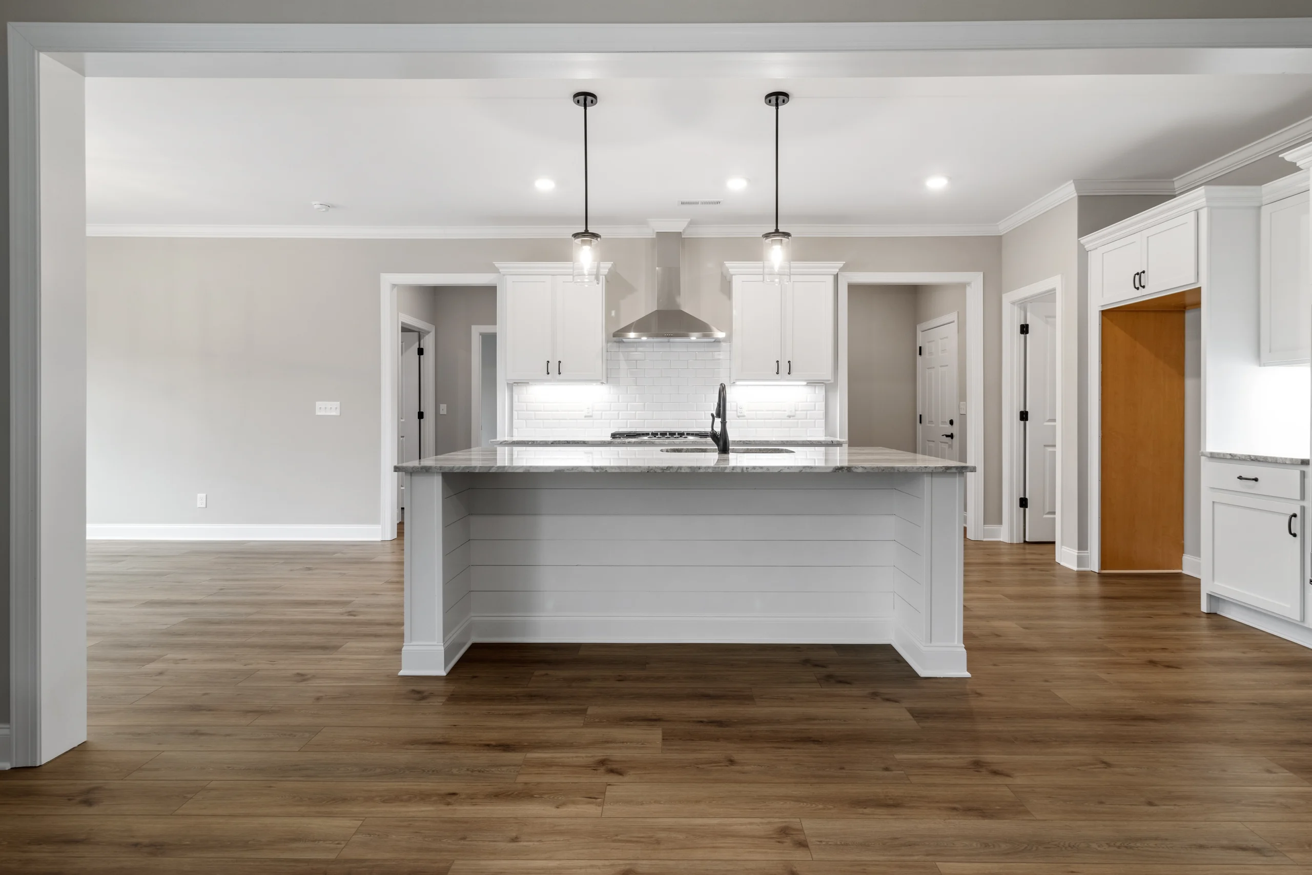 New Home Chattanooga TN. Spacious kitchen by Pratt Home Builders, featuring a large island, pendant lights, wood flooring, and white cabinetry.