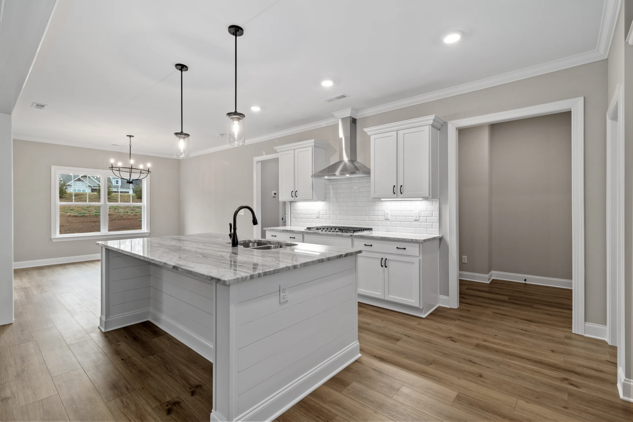New Home Chattanooga TN. Modern kitchen with marble island, pendant lights, white cabinets, and wooden floors by Pratt Home Builders.