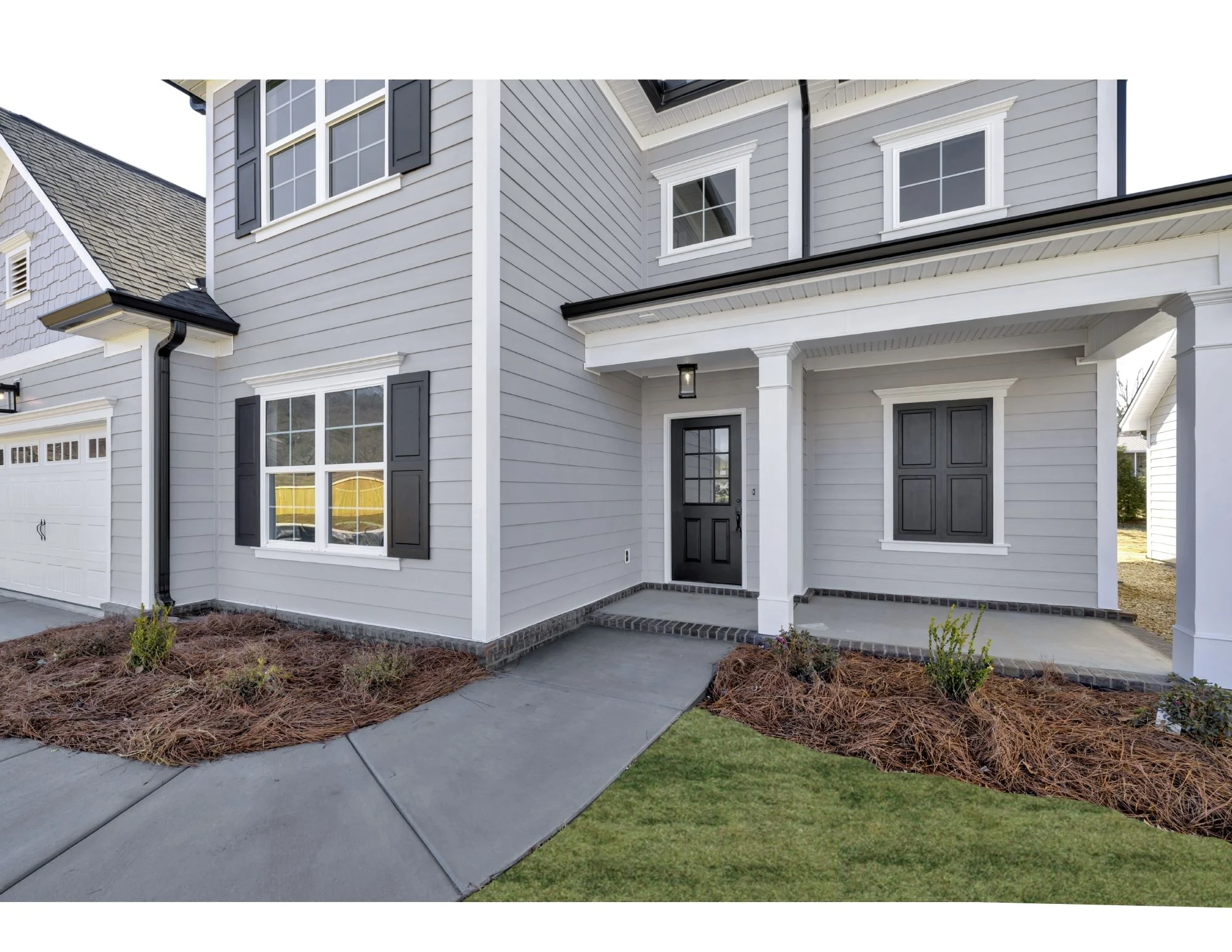 New Home Chattanooga TN. Modern gray home with black shutters, inviting porch, and neat landscaping by Pratt Home Builders. House features white trim.
