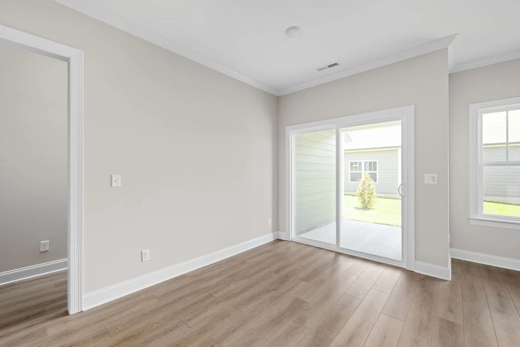 New Home Chattanooga TN. Spacious, sunlit room with light wood flooring, neutral walls, and a large sliding door leading to a patio. Built by Pratt Home Builders.