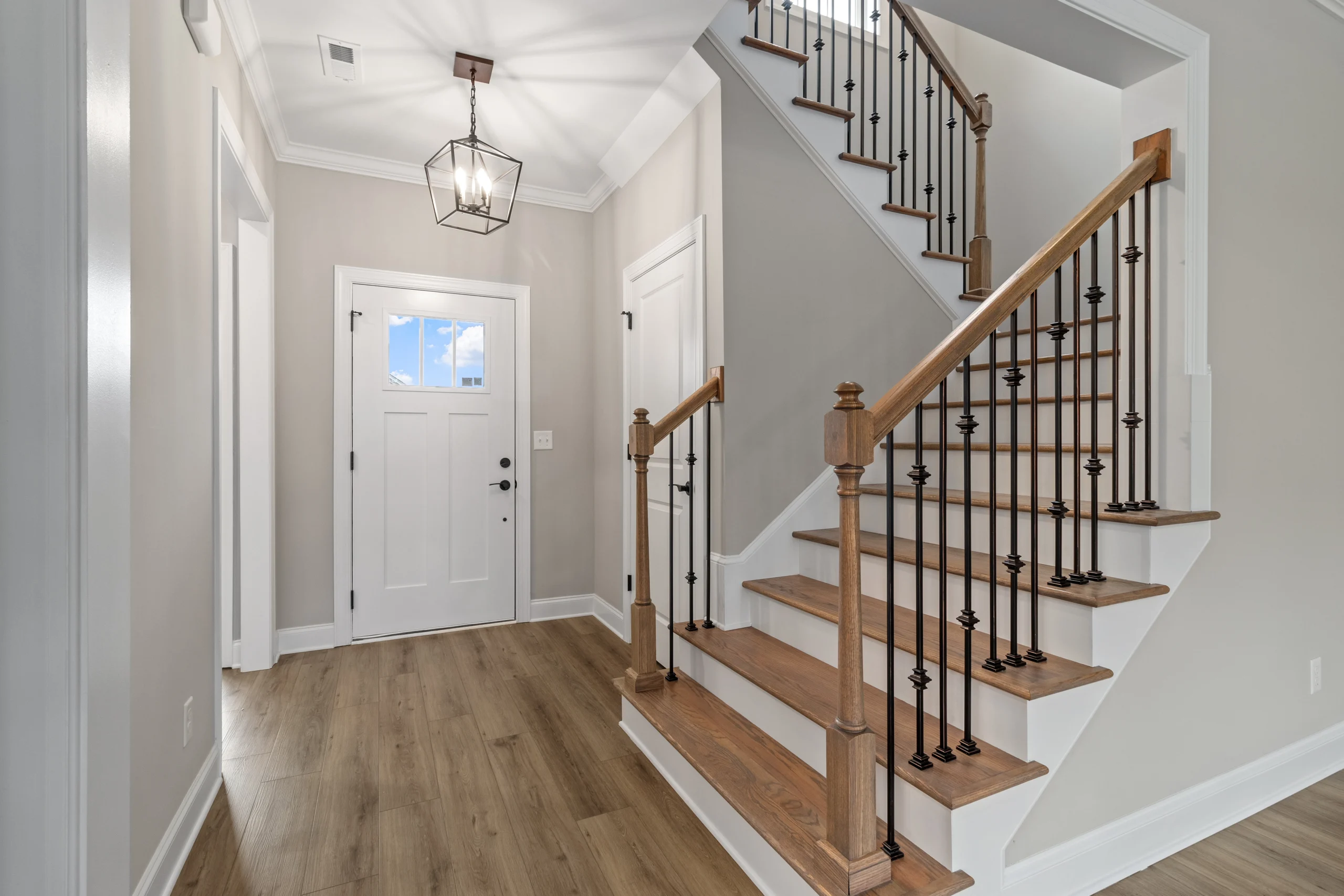 New Home Chattanooga TN. Spacious entryway with wooden stairs, iron railings, lantern light fixture, and white door. Designed by Pratt Home Builders.