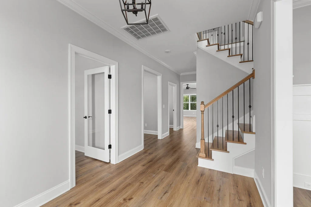 New Home Chattanooga TN. Bright hallway with wooden floors, white doors, and a modern staircase. Designed by Pratt Home Builders.