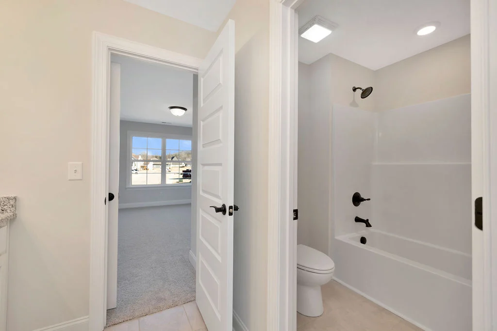 New home Chattanooga TN. Bathroom with white tub, dark fixtures, and adjoining carpeted room with large windows by Pratt Home Builders.