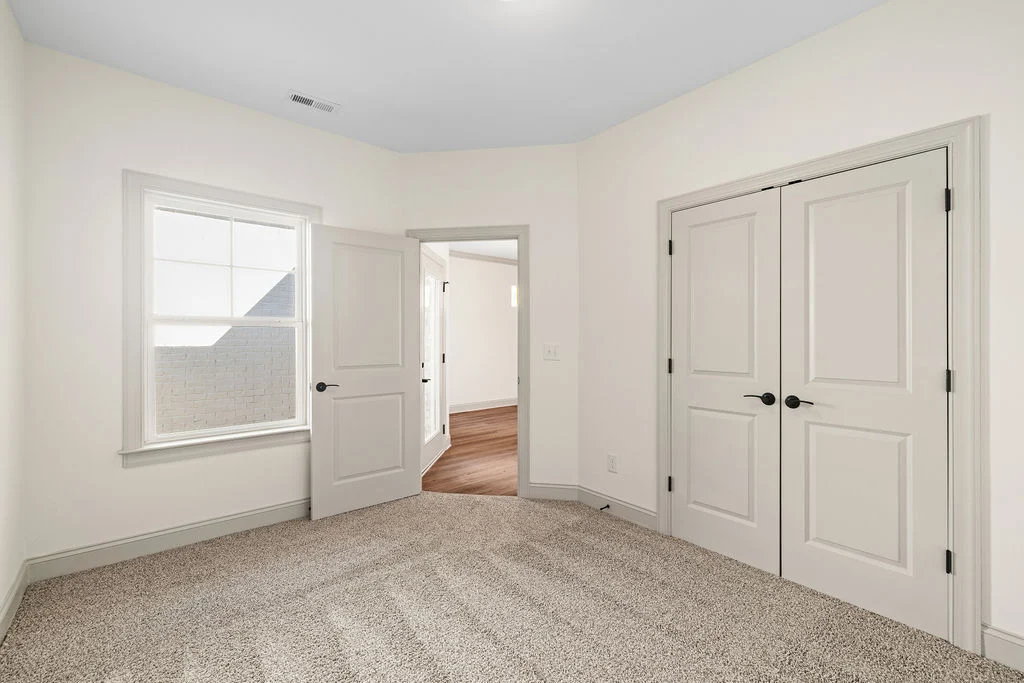 Bright room with beige carpet, large window, double closet doors, open door showing wooden floor hallway. Built by Pratt Home Builders in Chattanooga
