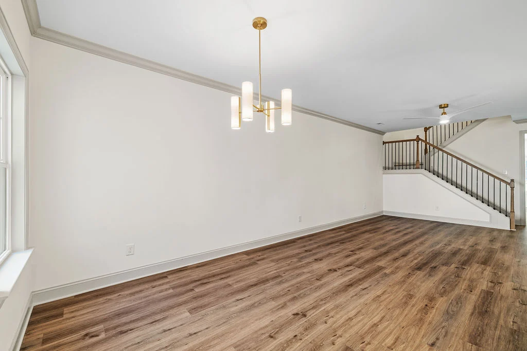 Modern living area with wooden floors, elegant chandelier, and staircase by Pratt Home Builders in Chattanooga, TN. Light, airy ambiance.