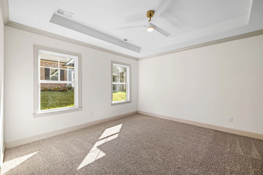 Bright, empty room with two windows, carpeted floor, and ceiling fan. Built by Pratt Home Builders in Chattanooga TN.