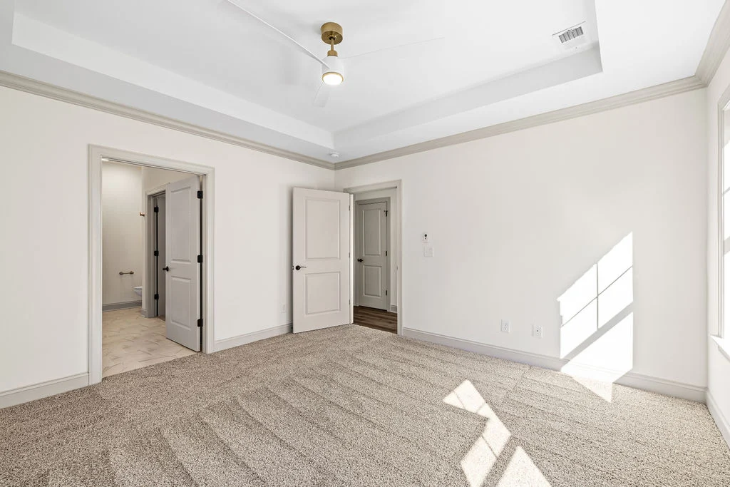 New Home Chattanooga TN. Spacious bedroom with beige carpet, tray ceiling, and natural light. Features double doors leading to a bathroom. Built by Pratt Home Builders.