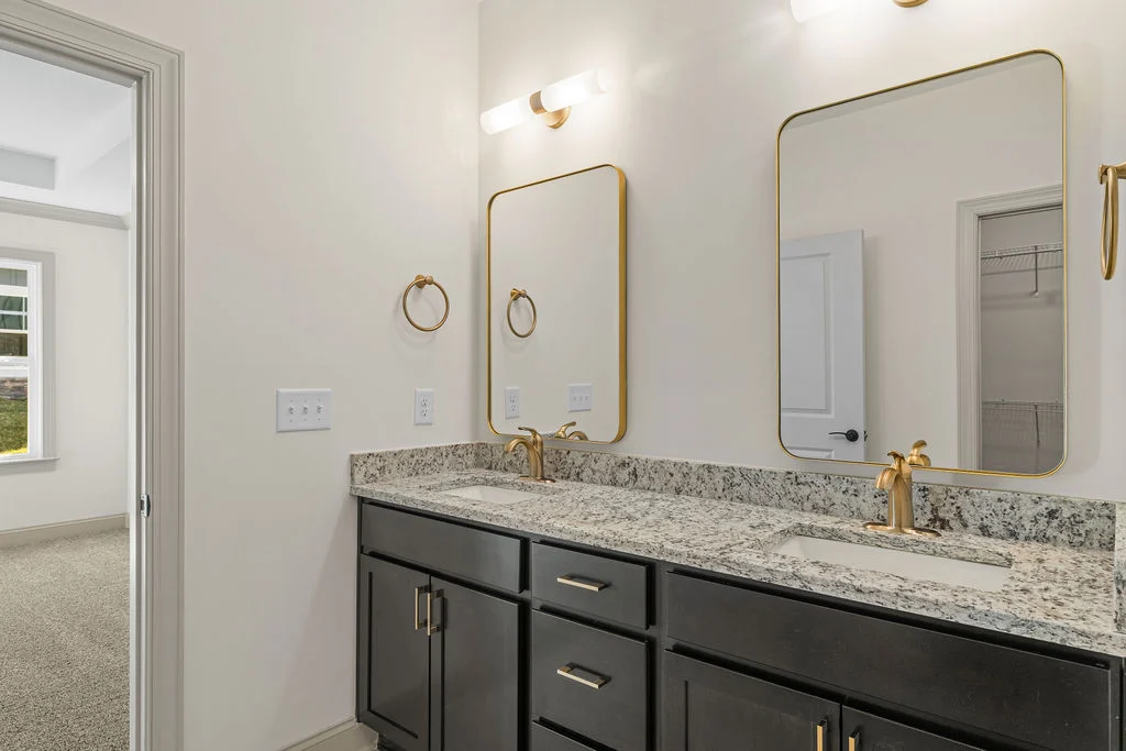 Modern bathroom with dual granite sinks, gold fixtures, and large mirrors, designed by Pratt Home Builders in Chattanooga TN.
