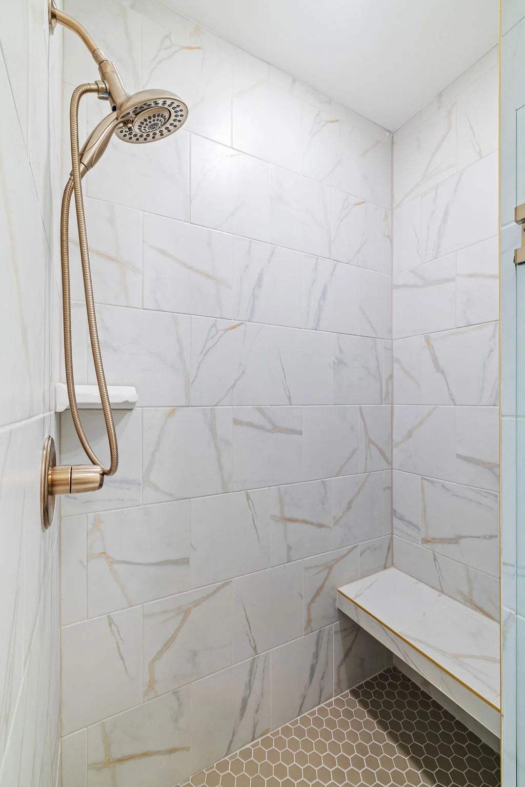 Modern shower with marble tile, brass showerhead, and built-in bench by Pratt Home Builders in Chattanooga TN.