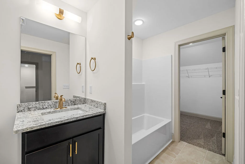 Modern bathroom by Pratt Home Builders in Chattanooga TN, featuring granite countertop, dark vanity, and adjacent walk-in closet.