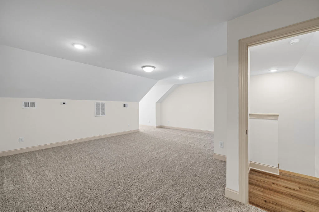 Spacious attic with neutral carpet, recessed lighting, and open staircase by Pratt Home Builders in Chattanooga TN.