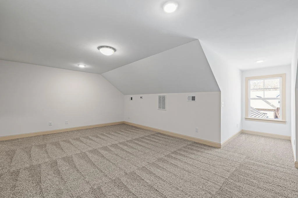 New Home Chattanooga TN. Spacious carpeted room with slanted ceiling, bright window, and modern lighting, designed by Pratt Home Builders.