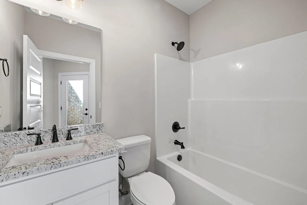 New Home Chattanooga TN. Modern bathroom with granite countertop, white cabinetry, and black fixtures by Pratt Home Builders. Bathtub and shower included.