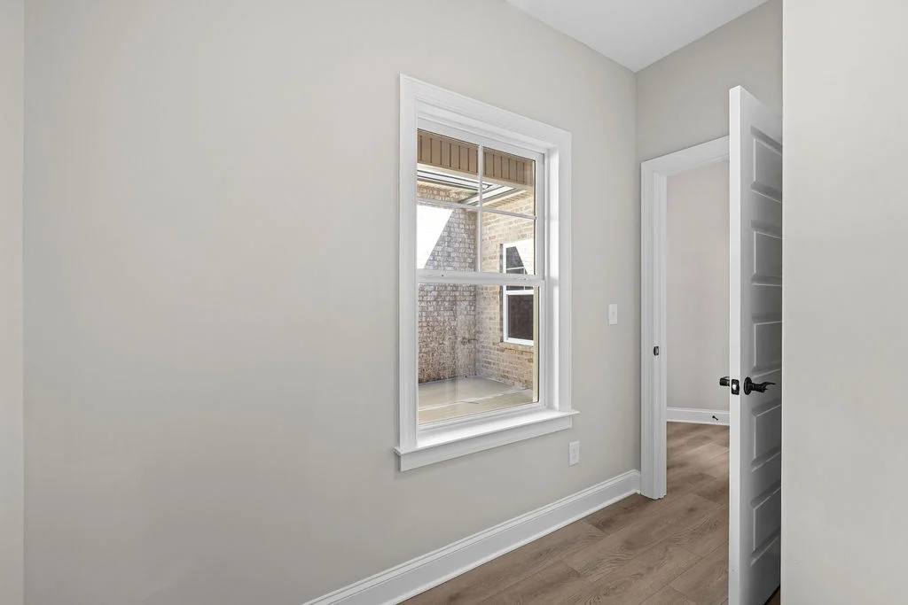 Empty room with light wood flooring, white walls, and a window overlooking a brick exterior, designed by Pratt Home Builders in Chattanooga TN.