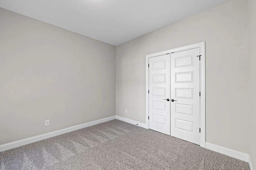 Empty room with light gray walls, white double doors, and carpet. New construction by Pratt Home Builders in Chattanooga, TN.
