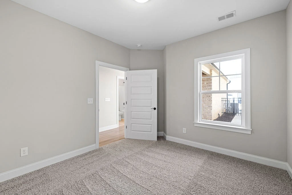 Empty room with beige walls, carpeted floor, open door, and window showing exterior. Built by Pratt Home Builders in Chattanooga TN.