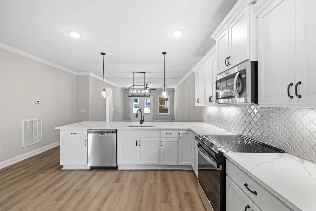 Modern kitchen with white cabinets, stainless steel appliances, pendant lighting, and a patterned backsplash, designed by Pratt Home Builders in Minne