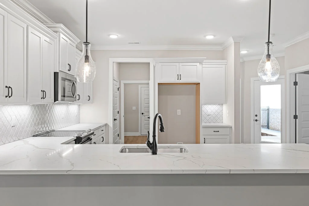 Modern kitchen by Pratt Home Builders in Chattanooga, TN, featuring white cabinets, marble countertops, stainless appliances, and pendant lighting.