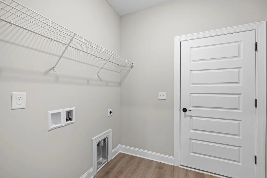 New Home Chattanooga TN. Laundry room with a white door, wire shelf, and plumbing hookups. Designed by Pratt Home Builders.