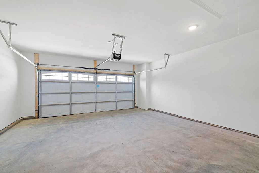 New home Chattanooga TN. Spacious two-car garage with concrete floor and white walls by Pratt Home Builders. Upper windows on closed garage doors.