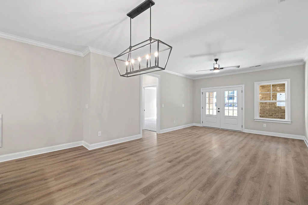 Spacious living room by Pratt Home Builders in Chattanooga TN, featuring light wood floors, modern chandelier, and dual glass doors.