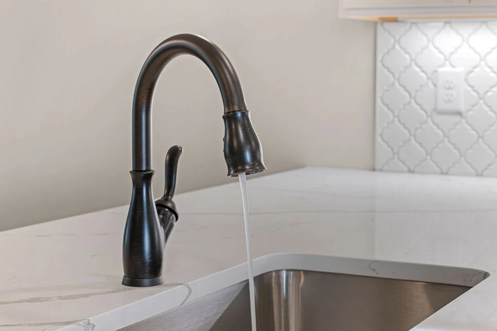 Bronze kitchen faucet over white marble countertop with tile backsplash; design by Pratt Home Builders in Chattanooga TN.