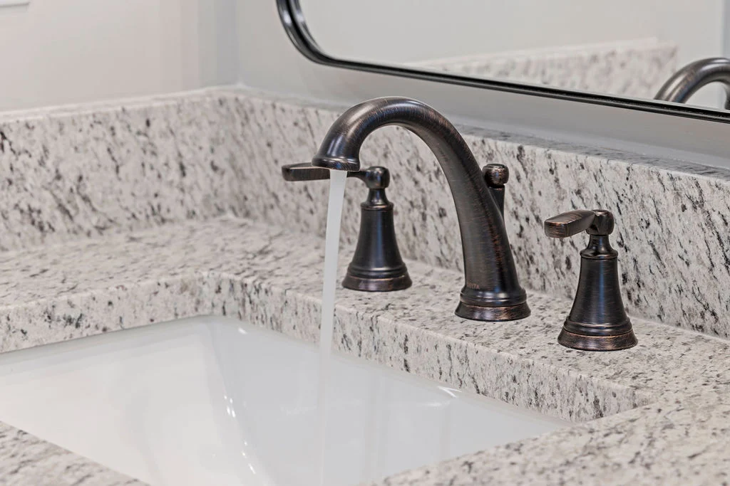 Bronze faucet with running water set in a granite countertop, reflecting Pratt Home Builders' design in Chattanooga, TN.