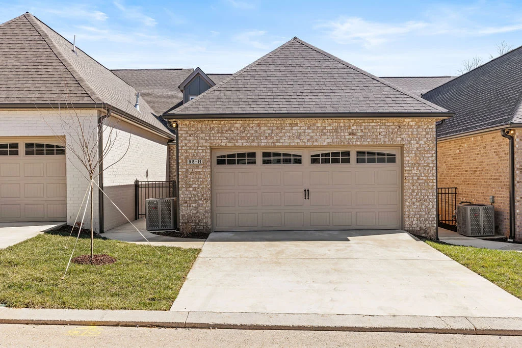 Two-car garage with brick facade, part of Pratt Home Builders in Chattanooga TN, featuring neatly trimmed grass and a young tree in front.