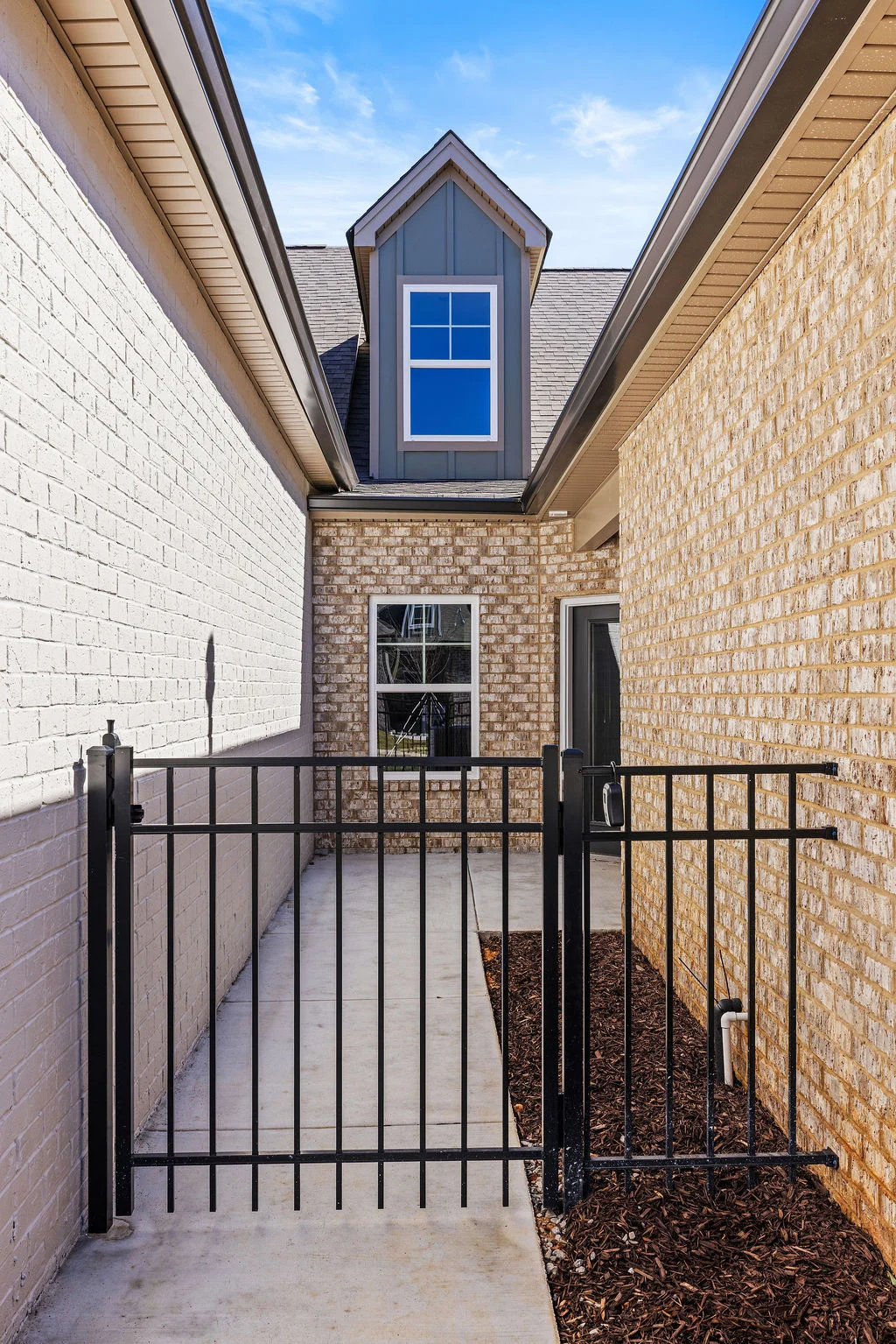 Gated entryway between brick walls leading to a modern windowed extension by Pratt Home Builders in Chattanooga TN.