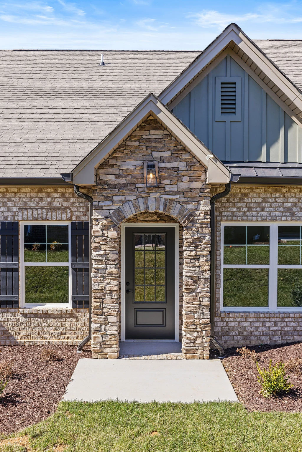 Elegant stone and brick facade with arched entryway and classic windows by Pratt Home Builders in Chattanooga TN. Lush greenery complements the design
