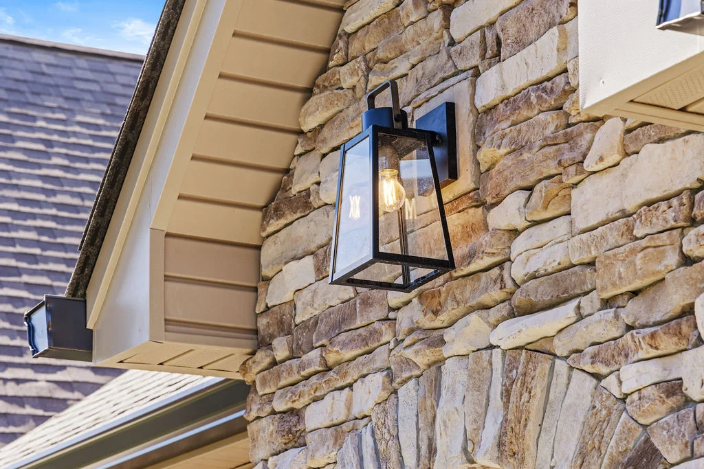 Rustic stone facade with a black lantern sconce on a Pratt Home Builders property, Chattanooga TN. Stone arch and roofline visible.