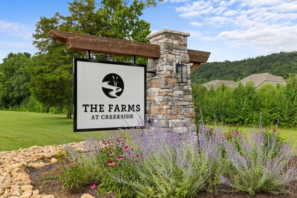 New Home Chattanooga TN. Stone sign for "The Farms at Creekside" amid vibrant landscaping, lush trees, and hills, by Pratt Home Builders.