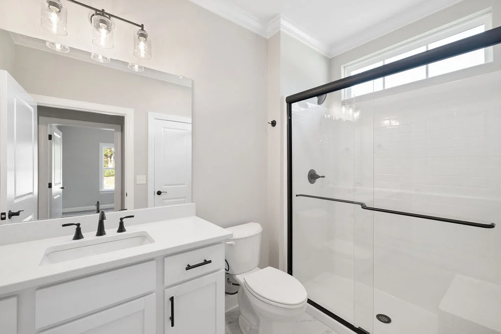 Modern bathroom with glass shower, black fixtures, and pristine white vanity. Pratt Home Builders in Chattanooga TN design.