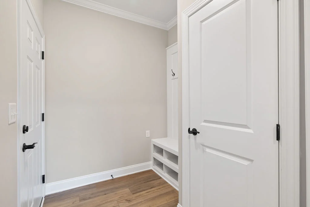 Entryway with white doors, wood floor, and a bench with shelving by Pratt Home Builders in Chattanooga, TN.