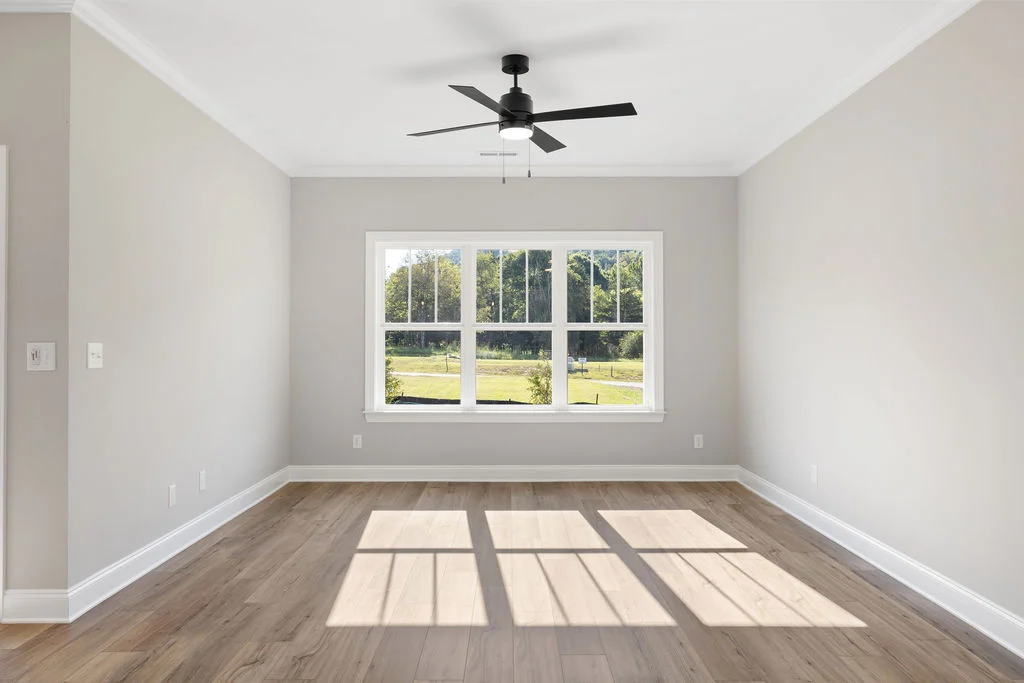 Bright, empty room with wood flooring, large window overlooking greenery, and ceiling fan. Designed by Pratt Home Builders in Chattanooga TN.