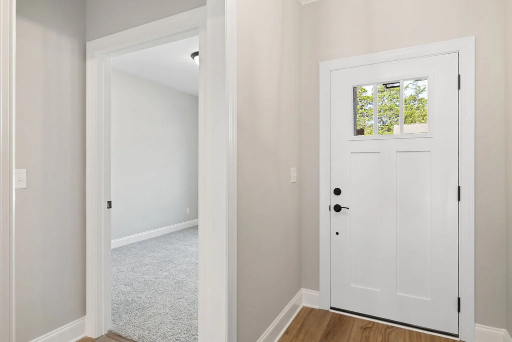 Bright entryway in a Pratt Home Builders home in Chattanooga, TN, featuring a white door with glass panes and adjacent carpeted room.