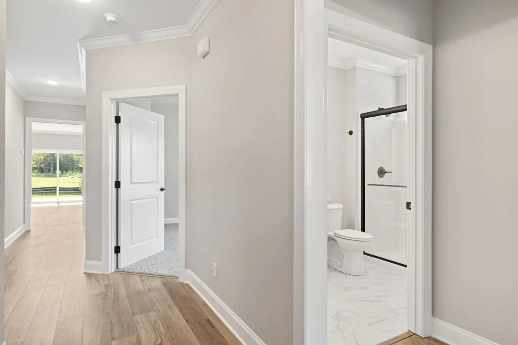 Hallway with light wood flooring, open doors to a room and bathroom, designed by Pratt Home Builders in Chattanooga TN.