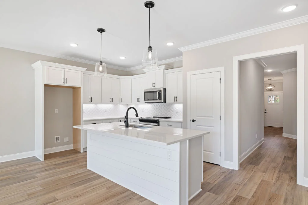 Modern kitchen with white cabinets, island, and pendant lights. Hardwood floors and recessed lighting by Pratt Home Builders in Chattanooga TN.