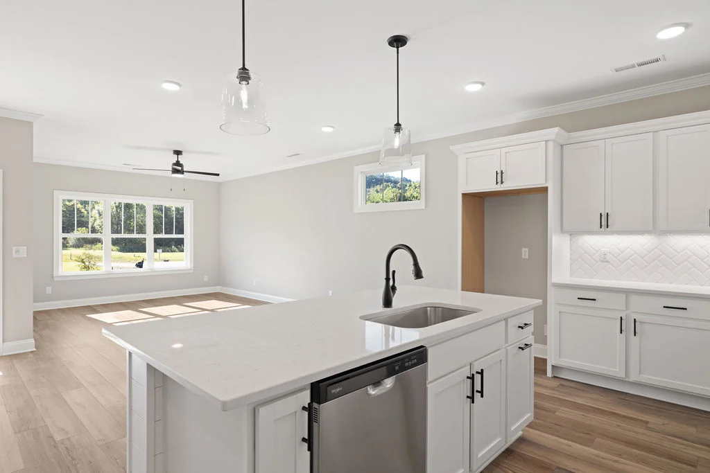 Modern kitchen and living area with white cabinets, island sink, wooden floors, and bright windows. Pratt Home Builders in Chattanooga TN design.