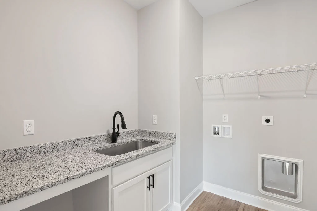 Modern laundry room with granite countertop, black faucet, wire shelf, and utility hookups by Pratt Home Builders in Chattanooga TN.