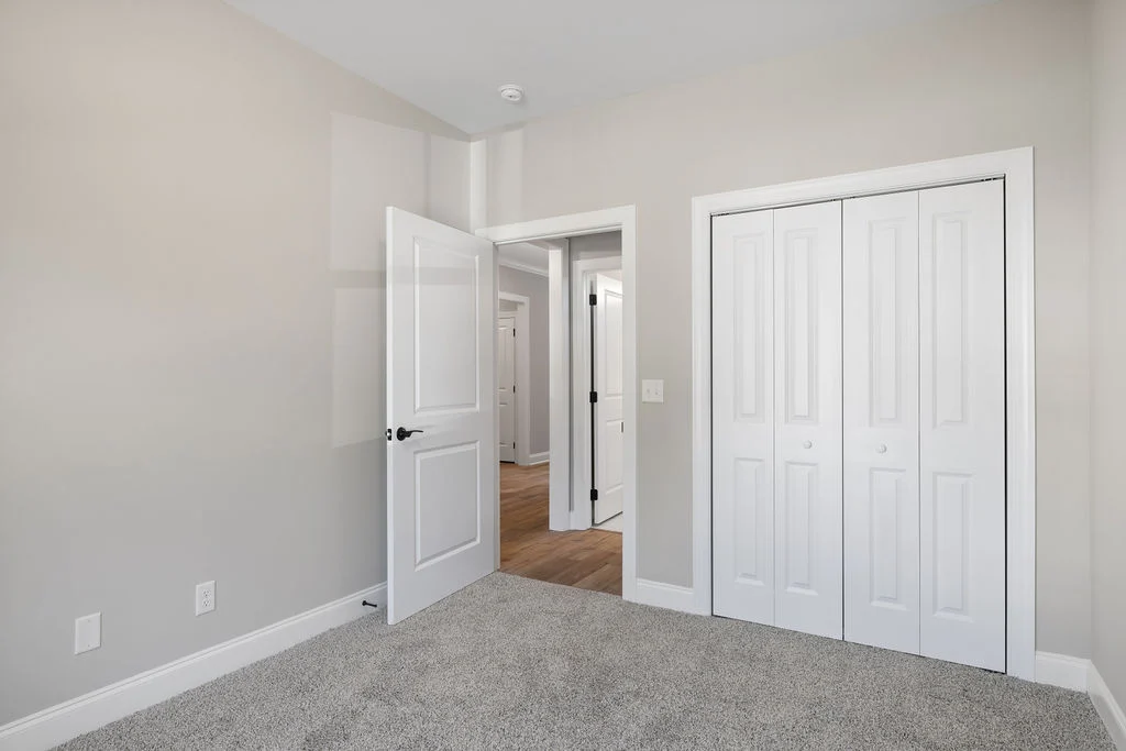 Neutral-toned room with carpet, closet, and open door revealing wood-floored hallway. Residential feature by Pratt Home Builders in Chattanooga TN.